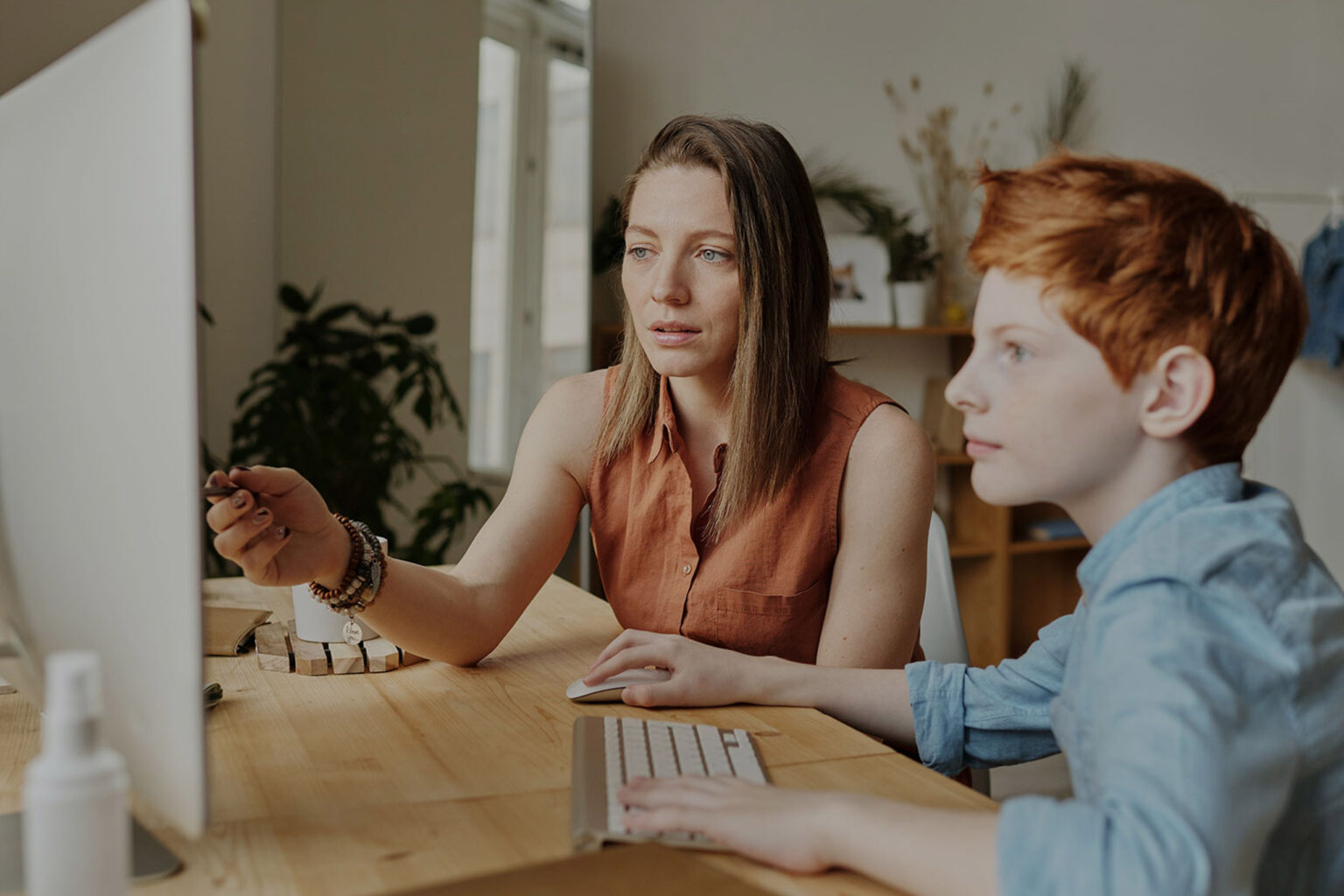 Eine Frau erklärt einem Jungen am PC-Monitor eine Aufgabe