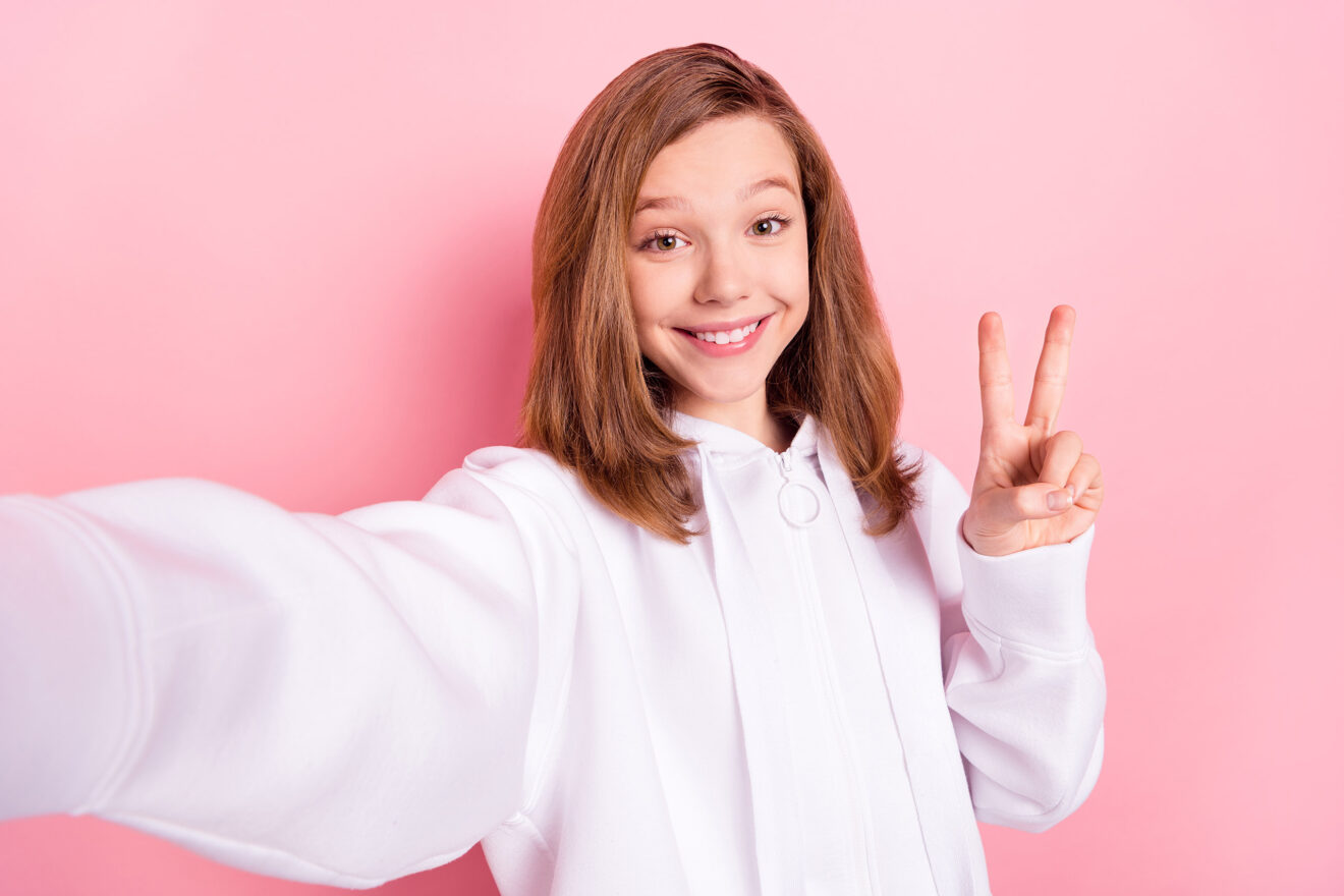 Ein junges Mädchen lacht in die Kamera und zeigt das Friedenszeichen